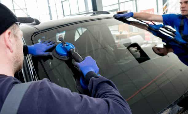 Automobile special workers replacing windscreen or windshield of a car in auto service station garage. Background